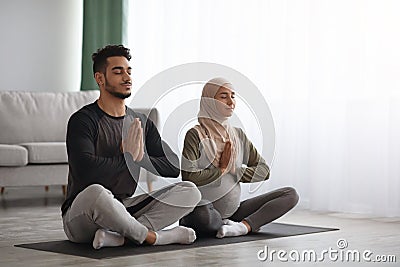Pregnant Muslim Woman In Hijab Meditating Together With Her Husband At Home Stock Photo