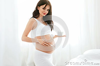 Pregnant Skin Care. Beautiful Woman Applying Cream On Belly Stock Photo