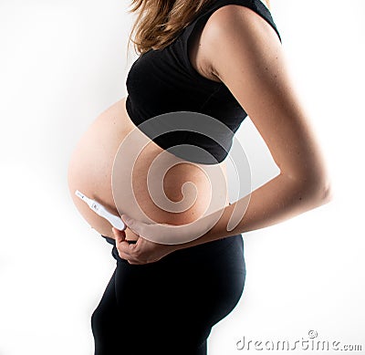 Pregnant skinny slim fit woman holding a positive pregnancy test on her belly tummy abdomen Stock Photo