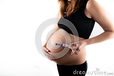 Pregnant skinny slim fit woman holding a positive pregnancy test on her belly tummy abdomen Stock Photo