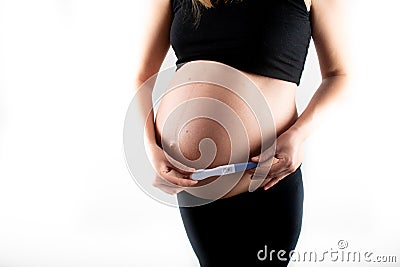 Pregnant skinny slim fit woman holding a positive pregnancy test on her belly tummy abdomen Stock Photo