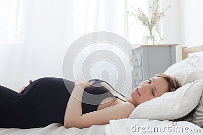 Pregnant smiling female lying on bed Stock Photo