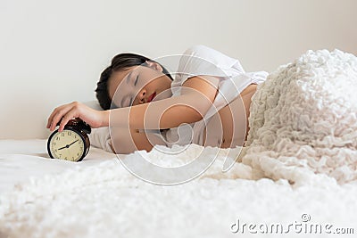 Pregnant teen woman lying in a white bed, is using her hands Press stop noise from alarm clock Stock Photo