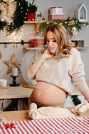 pregnant woman with a bare stomach in the New Year& x27;s kitchen. preparation dough Stock Photo