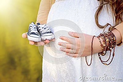 Pregnant woman belly holding baby booties. Stock Photo