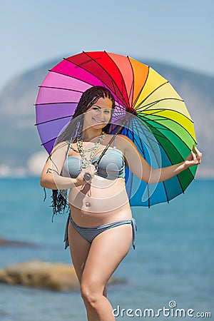 Pregnant woman in bikini with iridescent parasol against sea Stock Photo