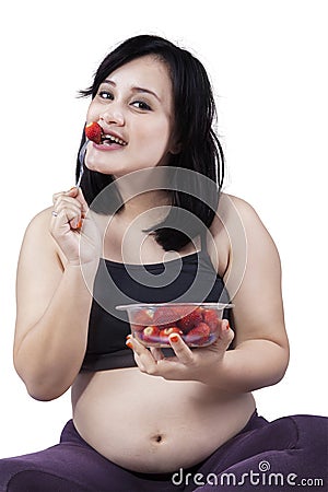 Pregnant woman bitting strawberry in studio Stock Photo