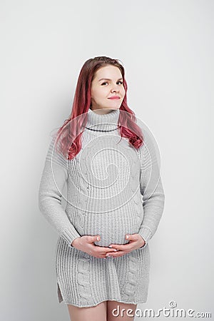 A pregnant woman with colored crimson hair in a knitted gray pullover. Stock Photo