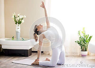 Pregnant woman doing ustrasana yoga pose at home Stock Photo