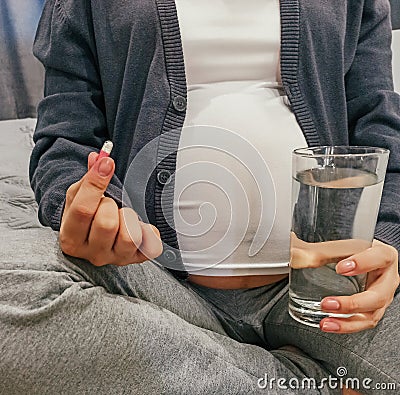 Pregnant woman drinks a pill with water Stock Photo