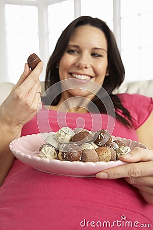 Pregnant Woman Eating Chocolates Sitting On Sofa At Home Stock Photo