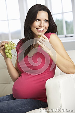 Pregnant Woman Eating Grapes Sitting On Sofa At Home Stock Photo