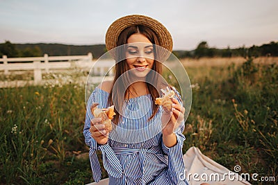 Pregnant woman in the field eating fresh backed crispy croissant. Healthy food. Young woman eats very appetizing Stock Photo