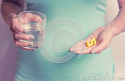 A pregnant woman first trimester in a blue T-shirt holds several medicine capsules, and in the second a glass of water. IVF. Stock Photo