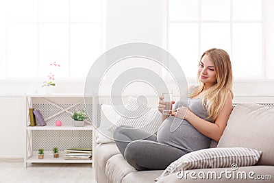 Pregnant woman with glass of water sitting on sofa Stock Photo