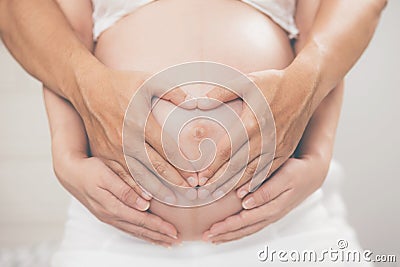 Pregnant woman and her husband hand splice hugging the tummy Heart shaped show love for the unborn baby in the belly relaxing at h Stock Photo