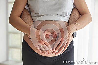 Pregnant woman and her husband make heart sind on belly Stock Photo