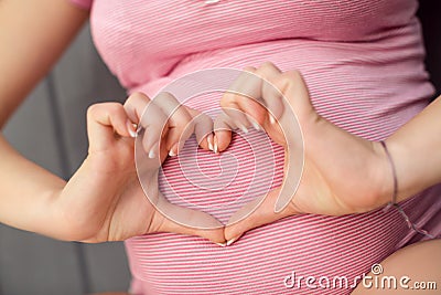Pregnant Woman holding her hands in heart shape on baby bump. Stock Photo