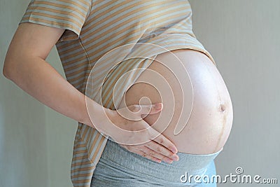 Pregnant Woman holding her right hand on her stomach takes side posture, reflective light from window to pregnant belly. Stock Photo