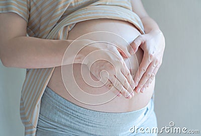 Pregnant Woman holding her right hand on her stomach takes side posture, reflective light from window to pregnant belly. Stock Photo