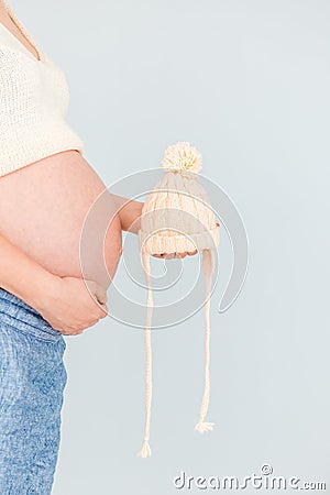 Pregnant woman is holding knitted beige children hat in front of her belly waiting for child& x27;s birth Stock Photo