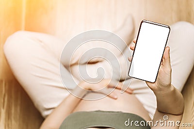 Pregnant woman holding a phone with a blank screen, mock-up. Pregnancy apps, gadgets, move and push tracking, diet Stock Photo