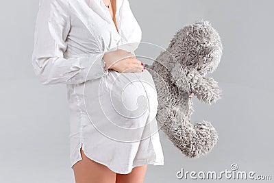 Pregnant woman holding soft toy. Pretty young woman carrying teddy bear. Stock Photo