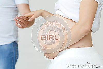 A pregnant woman holds her husband's hand on her stomach with the inscription - GIRL, a question mark Stock Photo