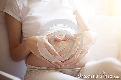 Pregnant woman lying in bed and touch her belly. Pregnancy heart shape at home, love sign Stock Photo