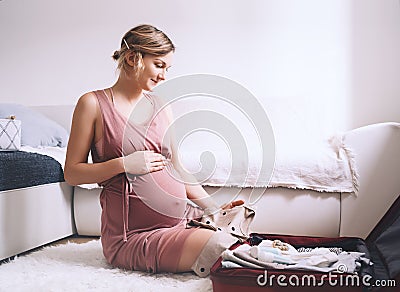 Pregnant woman is packing suitcase for maternity hospital getting ready for childbirth. Happy young mother with travel luggage of Stock Photo