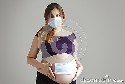 Pregnant woman in protective medical mask on face and on belly on isolated grey background, concept healthy pregnancy and Stock Photo