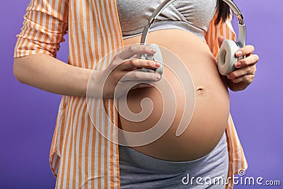 Pregnant woman puts headphones to abdomen in order her baby hear nature sounds Stock Photo