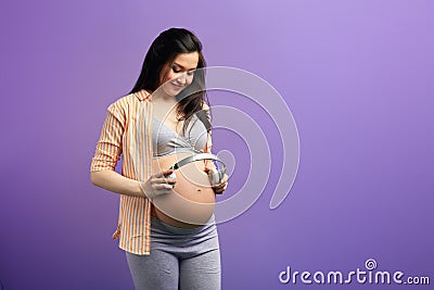 Pregnant woman puts headphones to abdomen in order her baby hear nature sounds Stock Photo