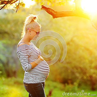 Pregnant woman on second trimester posing in sunny garden in the backlit Stock Photo