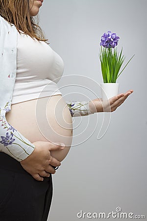 Pregnant woman showing belly in light colors holding a plant wit Stock Photo
