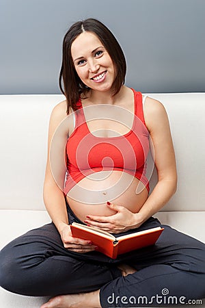 Pregnant woman sitting on sofa and holding book Stock Photo