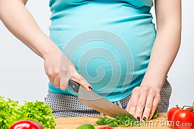 Pregnant woman slices fresh herbs on a cutting board Stock Photo