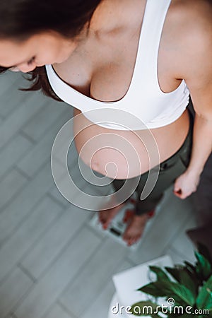 pregnant woman in sport white bra stand on scales measuring her weight at home. Stock Photo