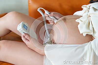Pregnant woman using fetal droppler device for listening baby heartbeat Stock Photo