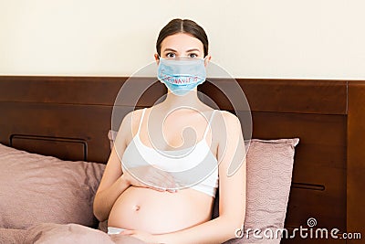 Pregnant woman is wearing protective medical mask with word. Mother is staying in bed because of respiratory disease. Stock Photo