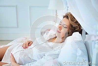 Pregnant woman in white blouse lying on bed. Sleap Stock Photo