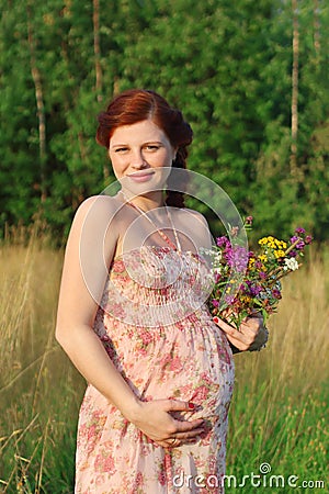 Pregnant woman with wild flowers touches belly at summ Stock Photo