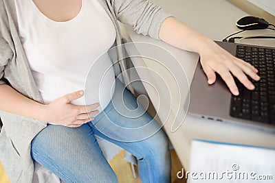 Pregnant woman working on laptop at her working place in office. Medical insurance childbearing. Maternity leave. Pregnancy and Stock Photo