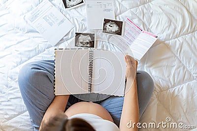 Pregnant woman writing list. Young pregnancy mother holding notepad. Pregnant lady writing check list of baby. Concept Stock Photo