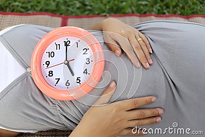 Pregnant women show clock on her belly to tell the time. Stock Photo