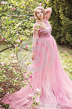 Pregnant young beautiful woman in pink lace long dress in a flowering garden Stock Photo