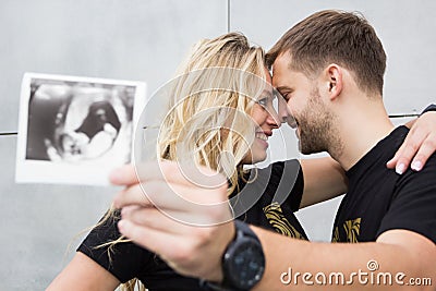 A pregnant young couple holds an ultrasound photograph of a child in their hands Stock Photo