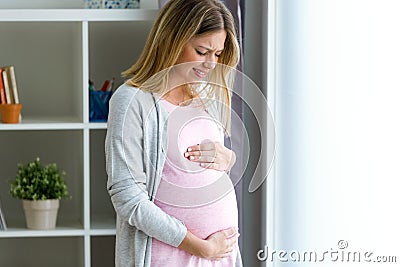 Pregnant young woman feels pain and stomachache and touching her belly at home. Stock Photo