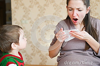 Pregnant young woman scared with nosebleed. A little boy looks at his pregnant mom. Healthcare and medical concept Stock Photo
