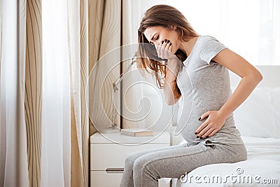 Pregnant young woman sitting on bed and feeling sick Stock Photo